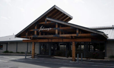 Wooden entrance canopy with metal brackets over a storefront, featuring glass doors beneath.