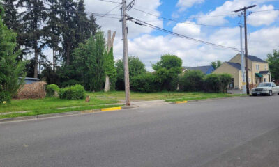 Suburban street with a grassy vacant lot on the left, a utility pole, and a house with a parked pickup on the right.