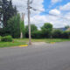 Suburban street with a grassy vacant lot on the left, a utility pole, and a house with a parked pickup on the right.