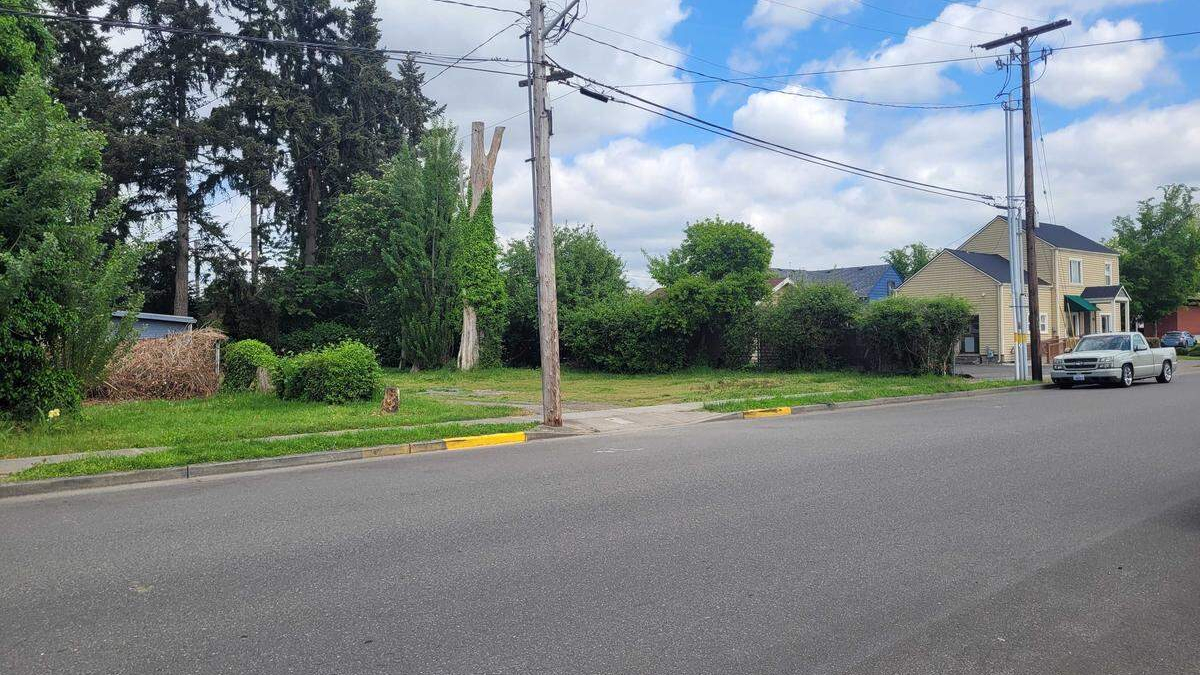 Suburban street with a grassy vacant lot on the left, a utility pole, and a house with a parked pickup on the right.