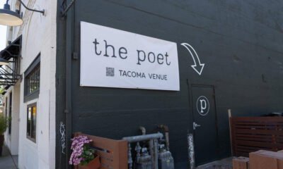 Exterior of The Poet Tacoma Venue: white sign on a dark wall, arrow pointing to a black door with a circular 'p' logo.