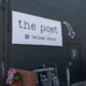 Exterior of The Poet Tacoma Venue: white sign on a dark wall, arrow pointing to a black door with a circular 'p' logo.