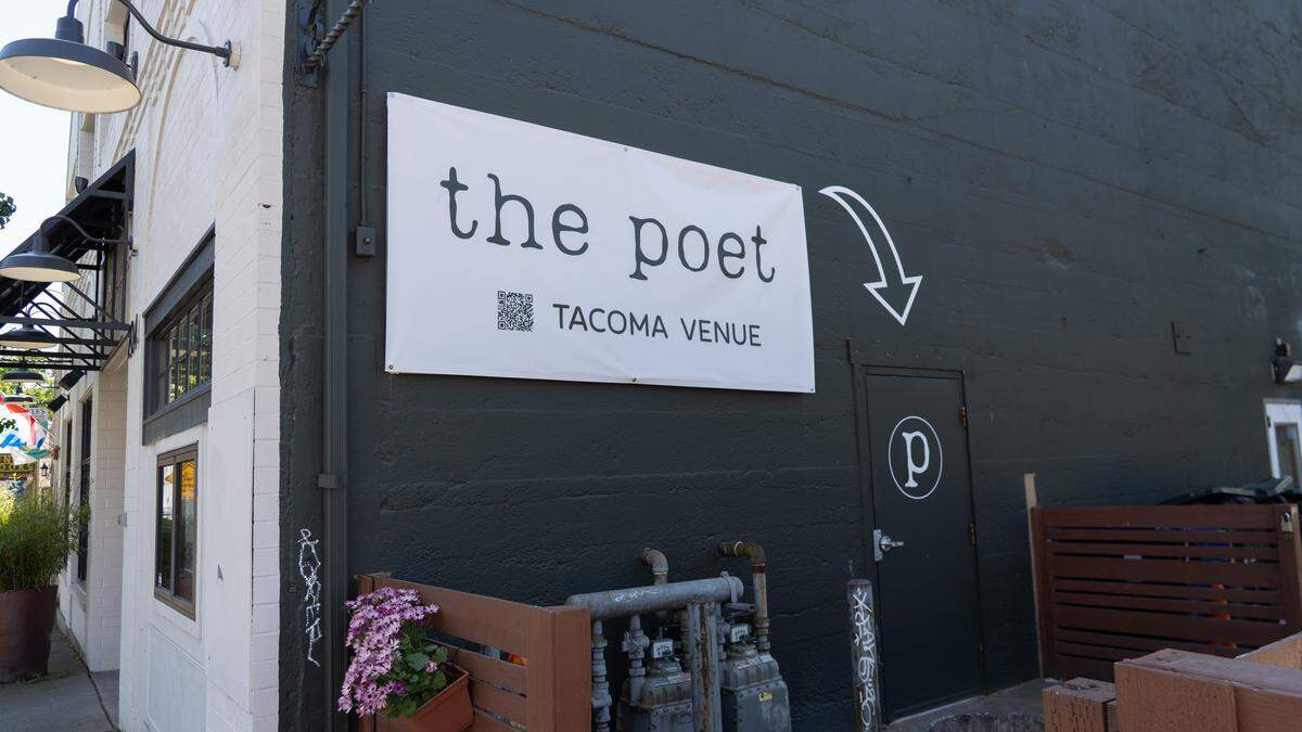 Exterior of The Poet Tacoma Venue: white sign on a dark wall, arrow pointing to a black door with a circular 'p' logo.