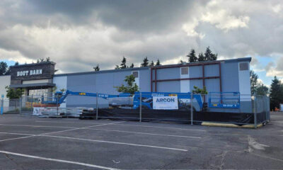 Boot Barn storefront under construction, construction equipment behind a chain-link fence in a parking lot under a cloudy sky.