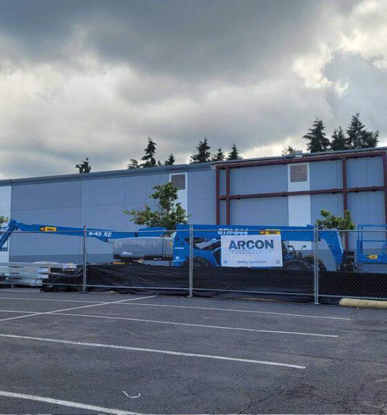 Boot Barn storefront under construction, construction equipment behind a chain-link fence in a parking lot under a cloudy sky.