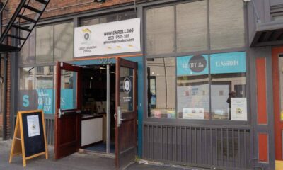 Open storefront of a learning center with a 'Now Enrolling' banner and blue window decals reading 'The City in a Classroom.'