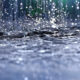 Close-up of raindrops striking a dark, choppy water surface with droplets suspended in midair.