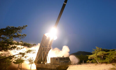 Mobile missile launcher on tracks fires a rocket into the dark sky, with bright exhaust and smoke surrounding the platform.