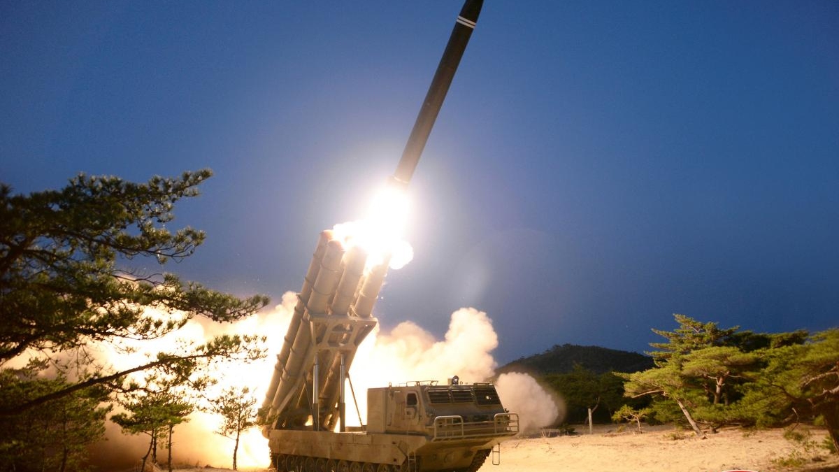 Mobile missile launcher on tracks fires a rocket into the dark sky, with bright exhaust and smoke surrounding the platform.