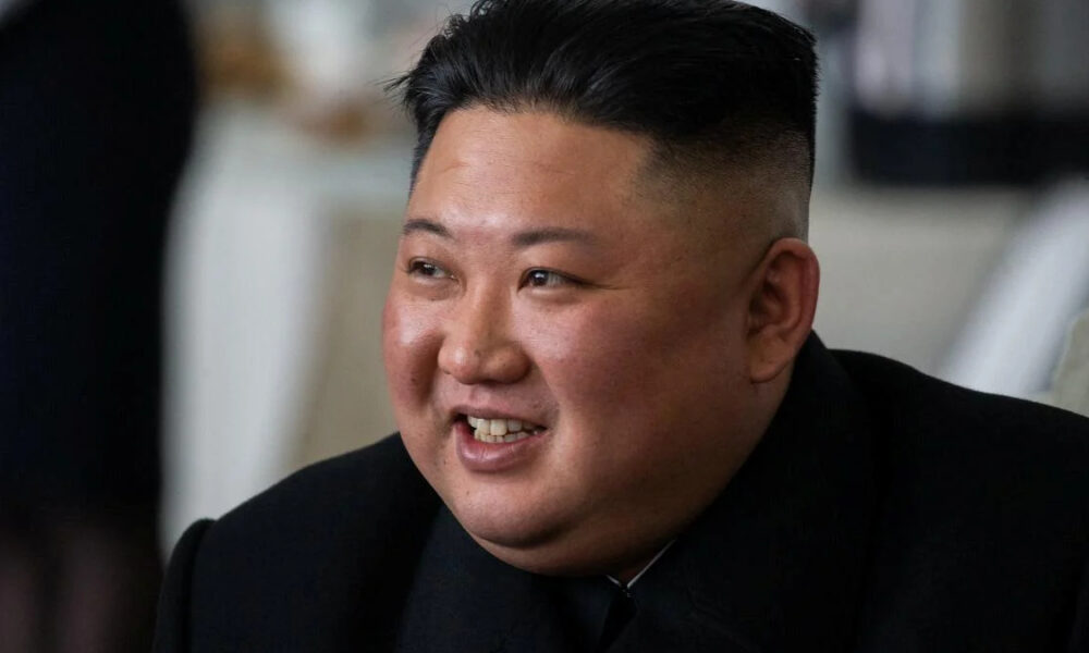 Close-up of a smiling man with a high fade haircut wearing a black suit indoors.