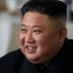 Close-up of a smiling man with a high fade haircut wearing a black suit indoors.