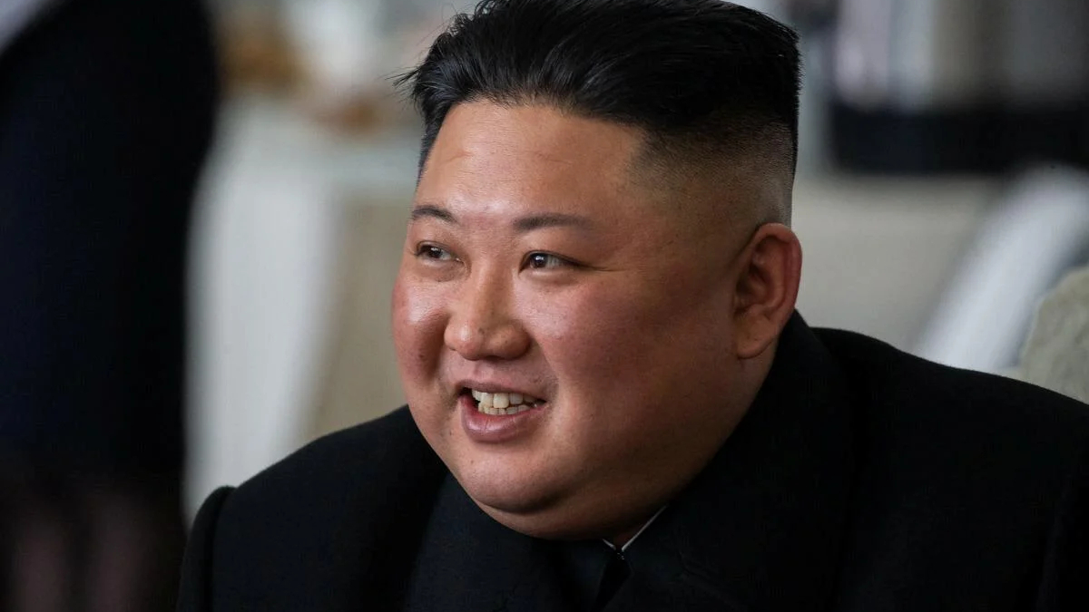 Close-up of a smiling man with a high fade haircut wearing a black suit indoors.