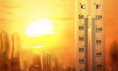 Thermometer showing high temperature beside a sunlit city skyline, suggesting a heatwave.