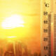 Thermometer showing high temperature beside a sunlit city skyline, suggesting a heatwave.