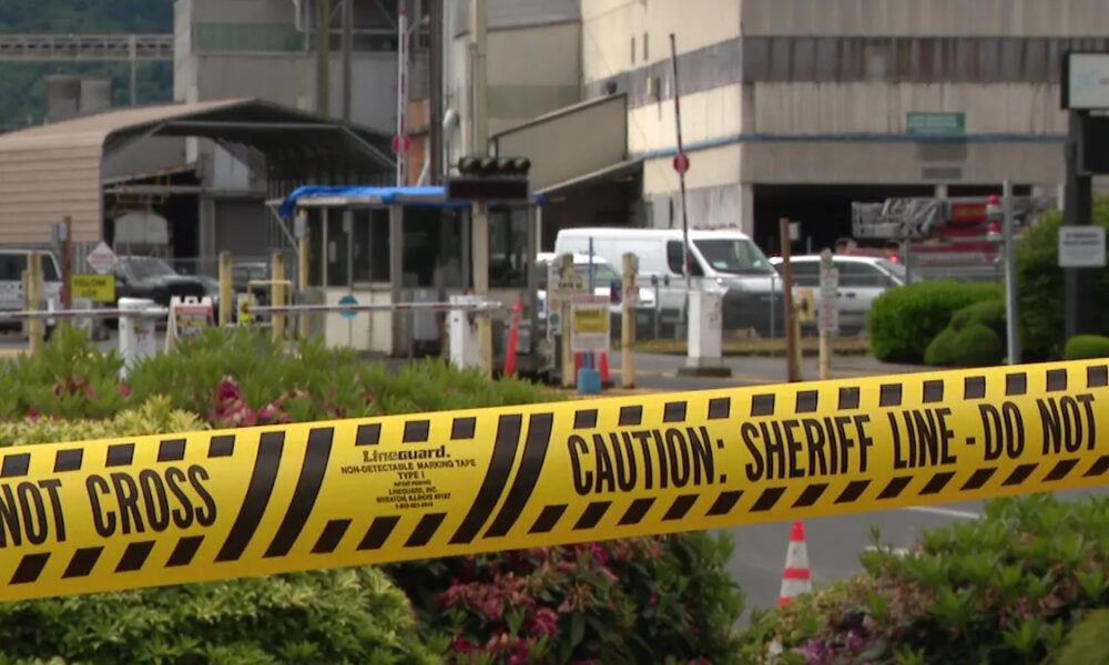 Yellow 'Do Not Cross' and 'Caution: Sheriff Line' tape in the foreground with a gated area and vehicles in the background, suggesting a restricted scene.