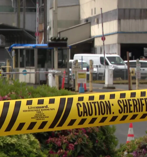 Yellow 'Do Not Cross' and 'Caution: Sheriff Line' tape in the foreground with a gated area and vehicles in the background, suggesting a restricted scene.
