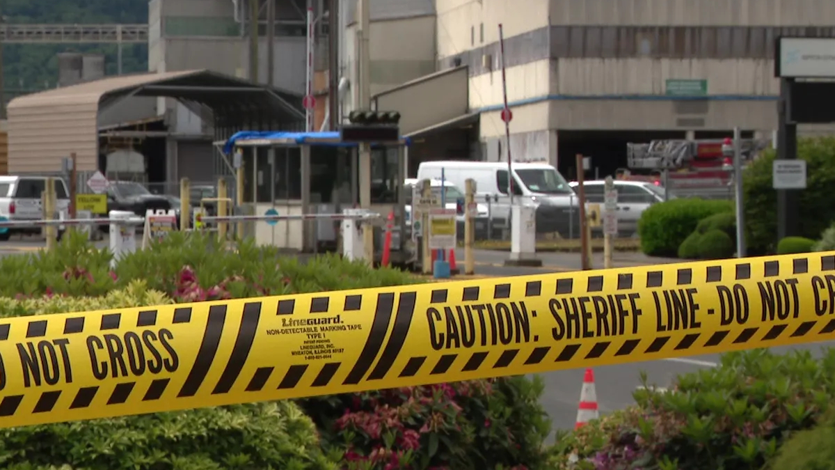 Yellow 'Do Not Cross' and 'Caution: Sheriff Line' tape in the foreground with a gated area and vehicles in the background, suggesting a restricted scene.