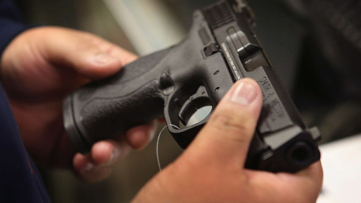 Close-up of a person gripping a black handgun with both hands, focusing on the grip and trigger area.