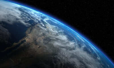 Curved view of Earth from space with a blue atmospheric rim and cloud cover against a starry background.