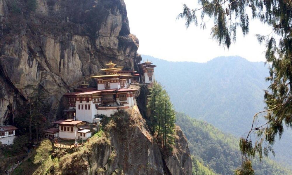 Tiger's Nest Monastery perched on a rocky cliff with pine trees and a forested valley in the distance.