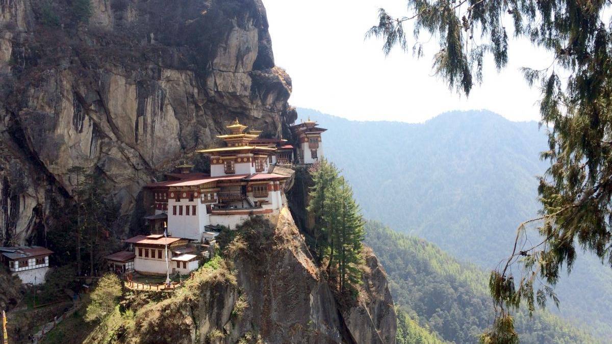 Tiger's Nest Monastery perched on a rocky cliff with pine trees and a forested valley in the distance.