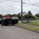 Black SUV resting on its side after a crash, with a red fire truck and firefighters at the scene in a residential street setting.