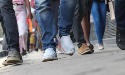 People walking on a city sidewalk, focusing on their varied shoes and legs in motion.