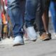People walking on a city sidewalk, focusing on their varied shoes and legs in motion.