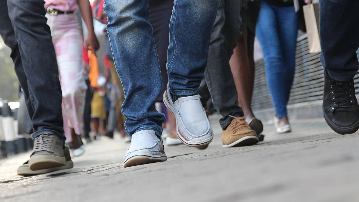 People walking on a city sidewalk, focusing on their varied shoes and legs in motion.