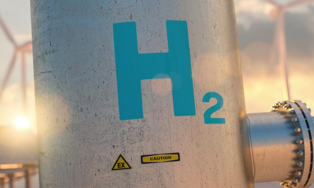 Industrial metal vessel with blue 'H2' label and caution EX signs in a sunny plant setting