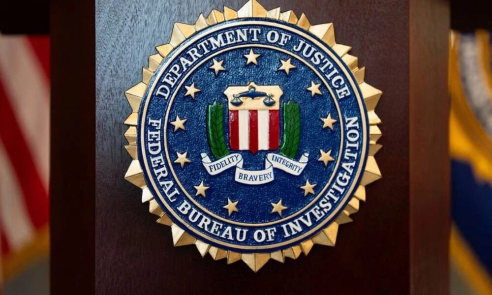 FBI seal mounted on a wooden podium with blurred American flags in the background.