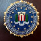 FBI seal mounted on a wooden podium with blurred American flags in the background.