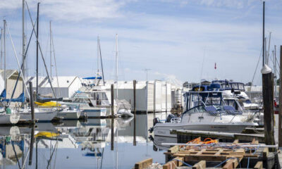Marina with sailboats and motor yachts docked along piers; calm water reflects hulls and masts.