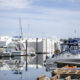 Marina with sailboats and motor yachts docked along piers; calm water reflects hulls and masts.