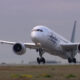 Alaska Airlines wide-body jet lifting off the runway, landing gear down, engines roaring against a cloudy sky.