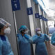 Healthcare workers in full PPE with masks and face shields standing in a corridor beside numbered bays 1–6.