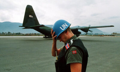 UN peacekeeper wearing a blue helmet on a tarmac with a military aircraft in the background