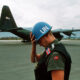 UN peacekeeper wearing a blue helmet on a tarmac with a military aircraft in the background