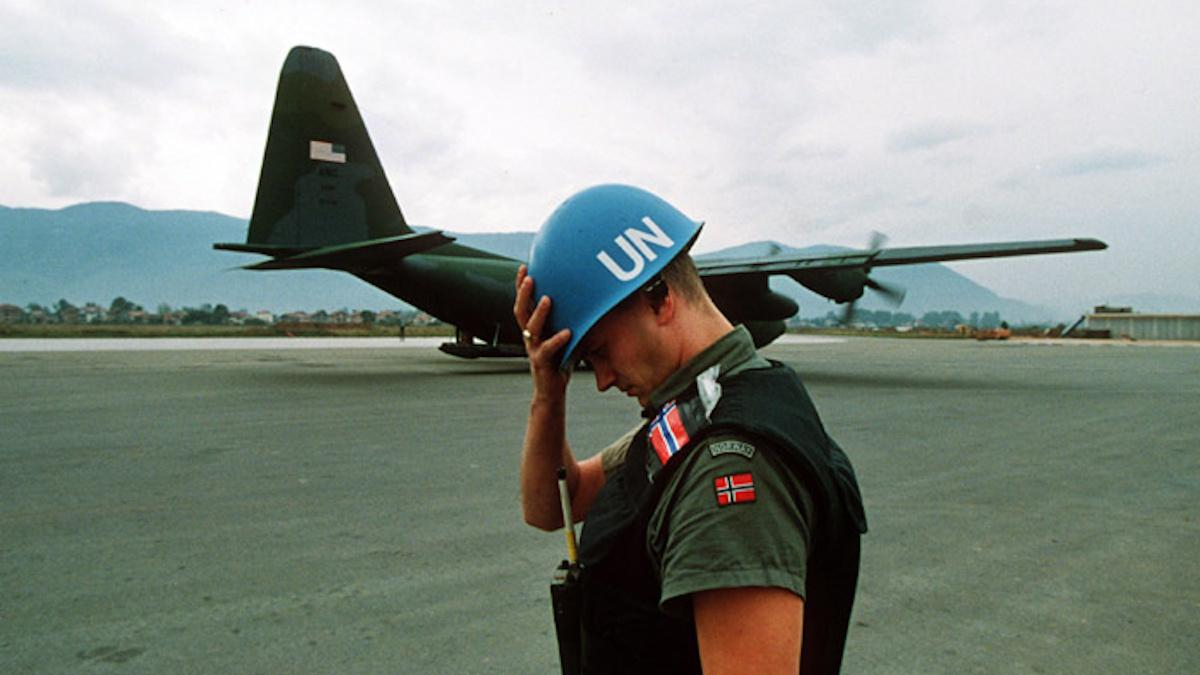 UN peacekeeper wearing a blue helmet on a tarmac with a military aircraft in the background