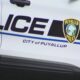 Puyallup Police car door with 'POLICE' lettering and city badge, blue stripe along white vehicle, partial American flag on rear edge.