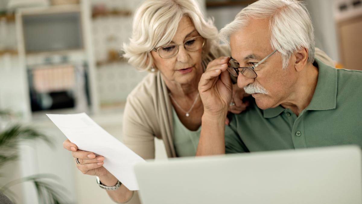 Older couple reviewing a printed document together while a laptop sits nearby.