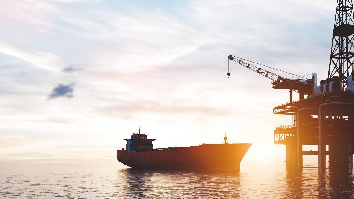 Cargo ship near an offshore oil platform at sunset, calm water reflecting warm light.