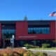 Front view of Swift Water Elementary School with red panels, large windows, and an American flag flying outside on a sunny day.