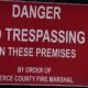 Red warning sign: "DANGER NO TRESPASSING ON THESE PREMISES" by order of Pierce County Fire Marshal on a dark background.