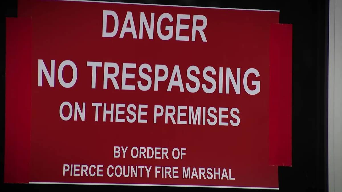 Red warning sign: "DANGER NO TRESPASSING ON THESE PREMISES" by order of Pierce County Fire Marshal on a dark background.