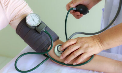 Healthcare professional measuring a patient's blood pressure with a cuff and stethoscope on the arm.