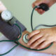 Healthcare professional measuring a patient's blood pressure with a cuff and stethoscope on the arm.