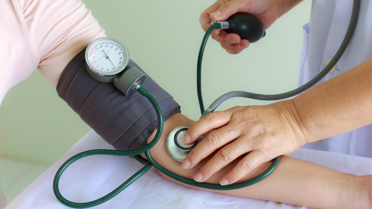 Healthcare professional measuring a patient's blood pressure with a cuff and stethoscope on the arm.