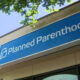 Blue storefront sign reading 'Planned Parenthood' on a building, with tree branches overhead.