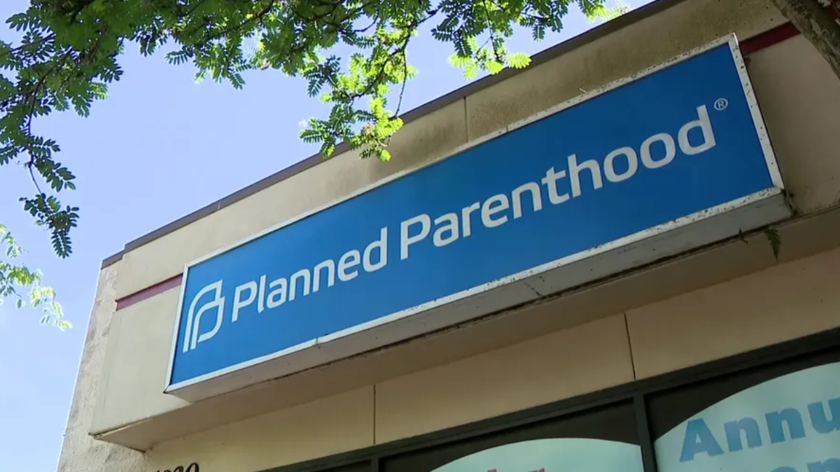 Blue storefront sign reading 'Planned Parenthood' on a building, with tree branches overhead.